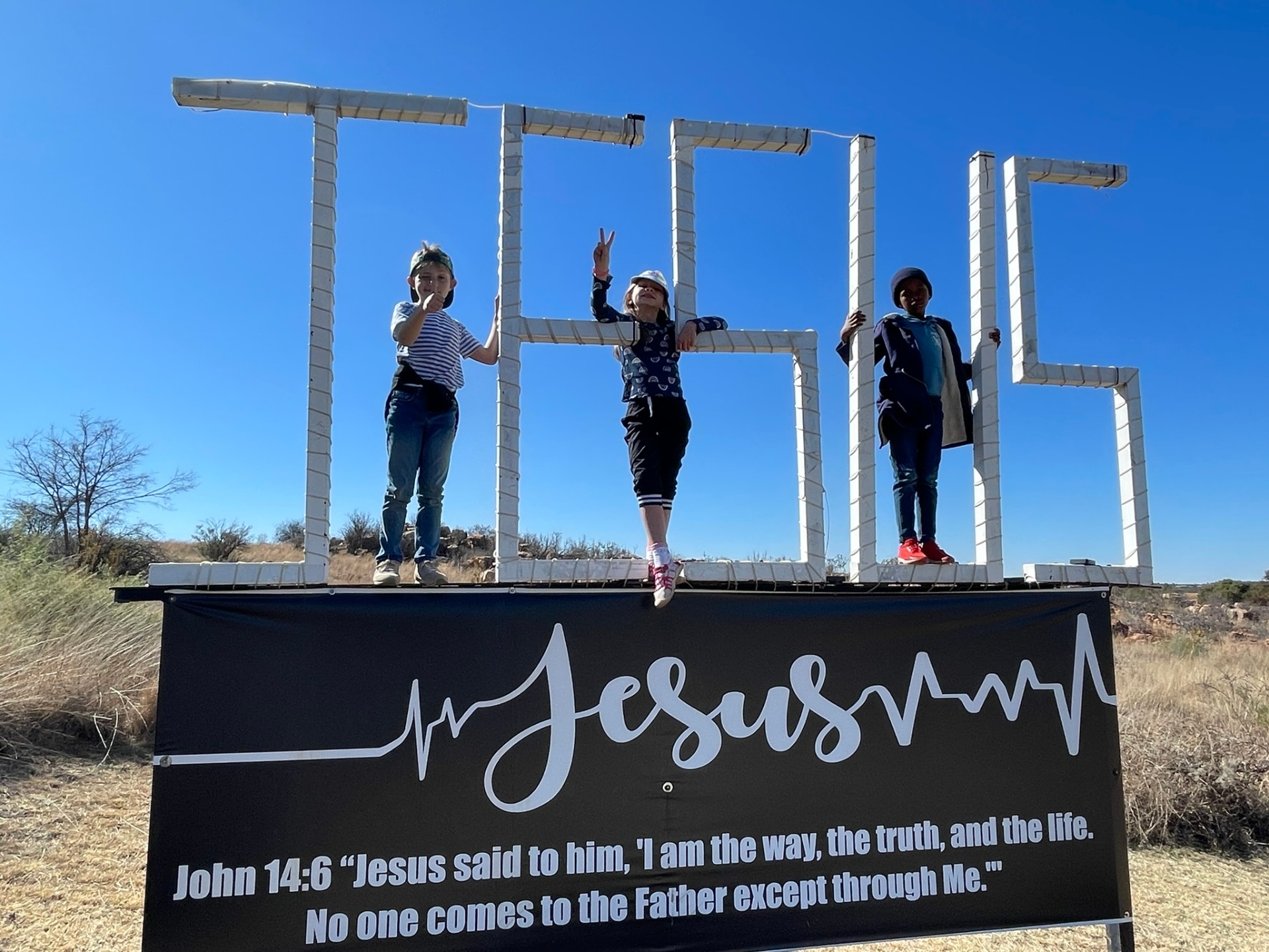 Three children standing on top of the JESUS sign