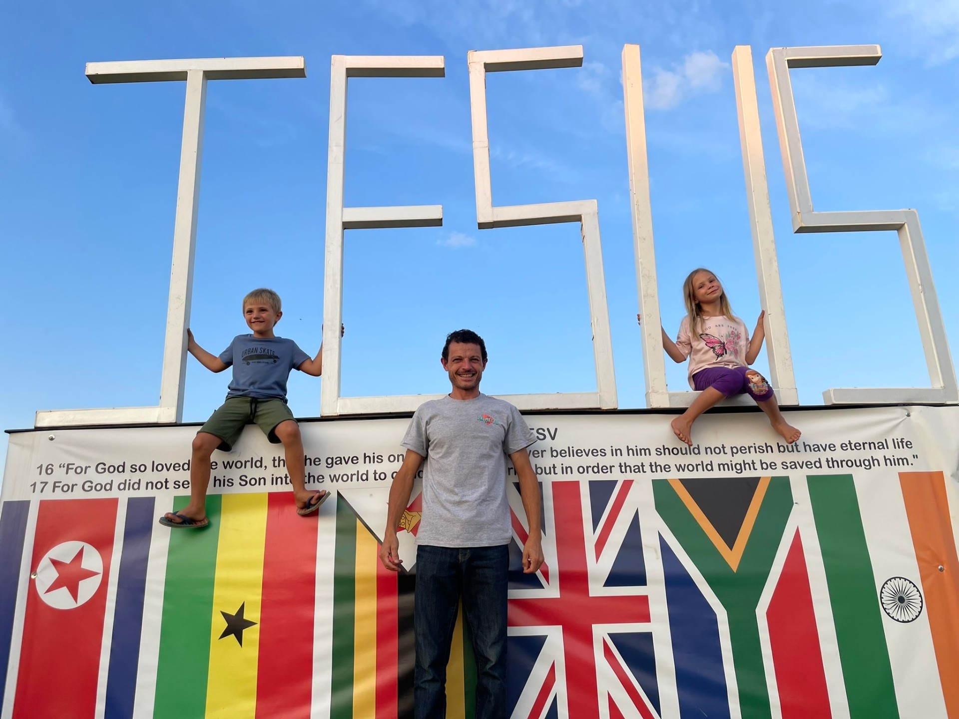 Dad with two kids on and beside the JESUS sign