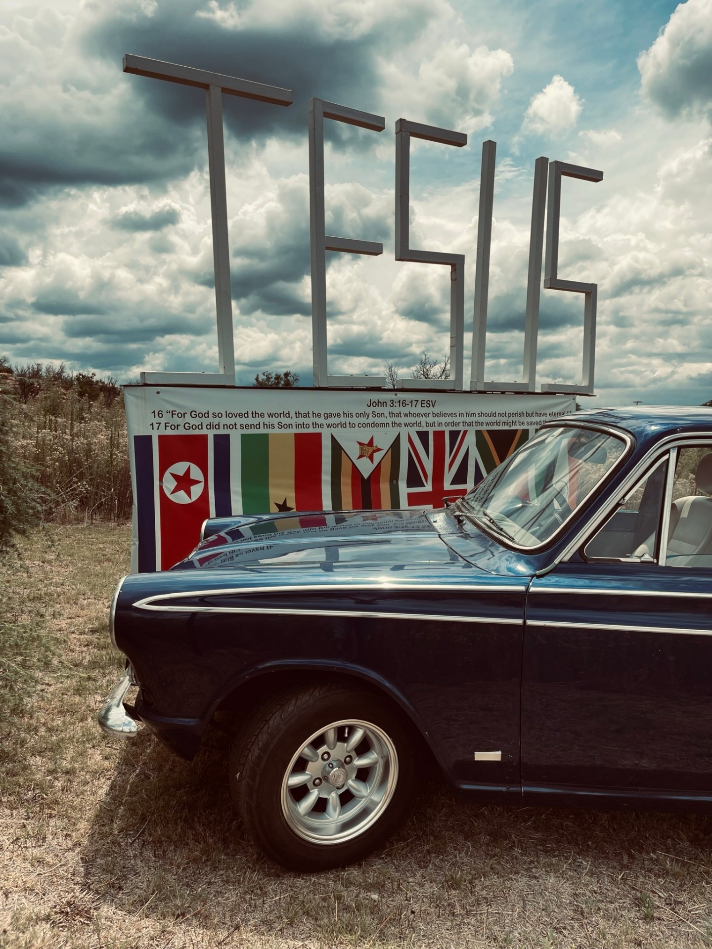 Classic blue Cortina parked beside the JESUS sign