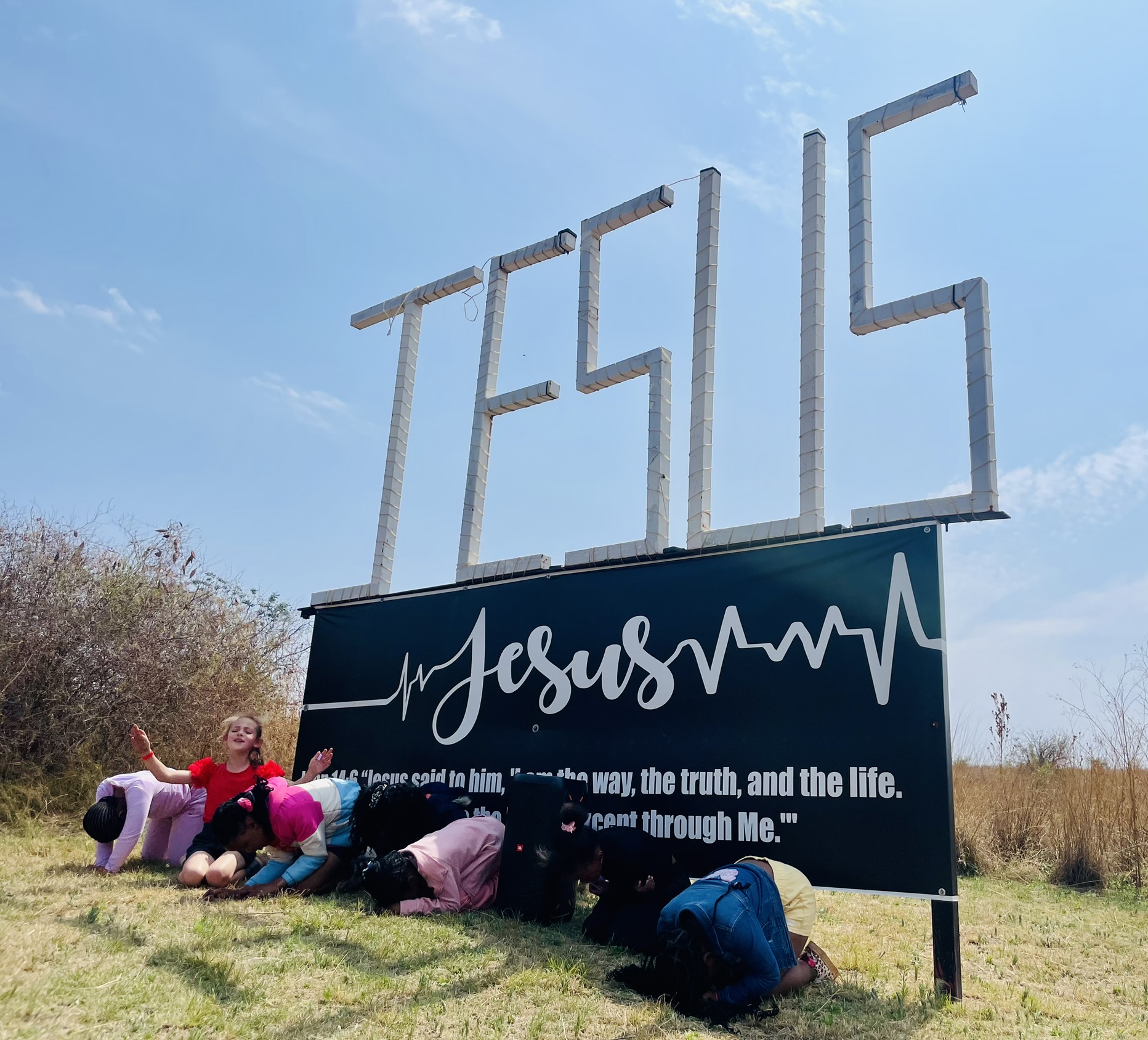 Children kneeling in prayer beneath the JESUS sign