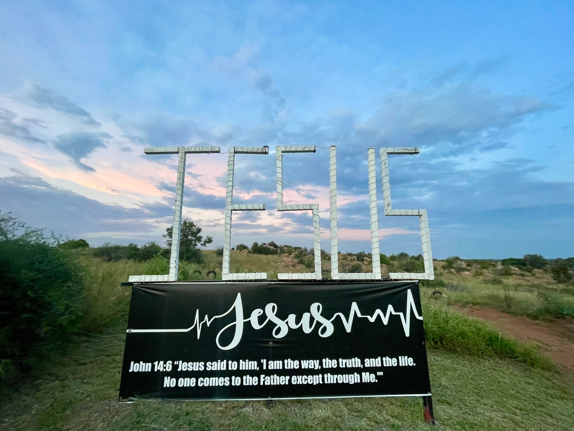 JESUS sign with John 14:6 banner against a soft sunset sky