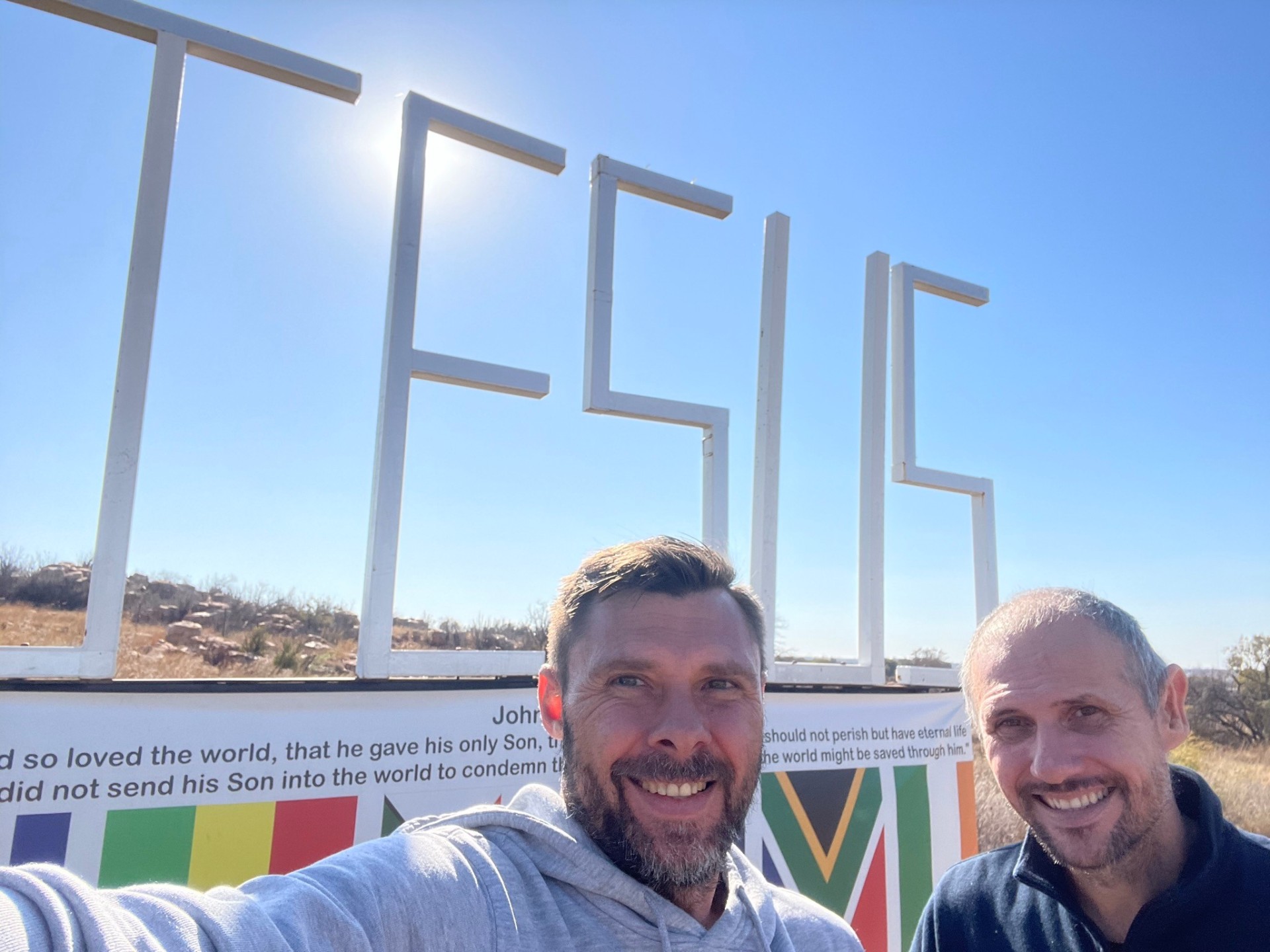 Two men taking a selfie in front of the JESUS sign
