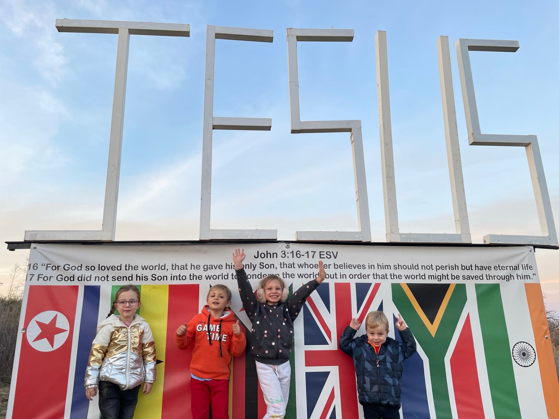 Four kids cheering in front of the JESUS sign and nations banner