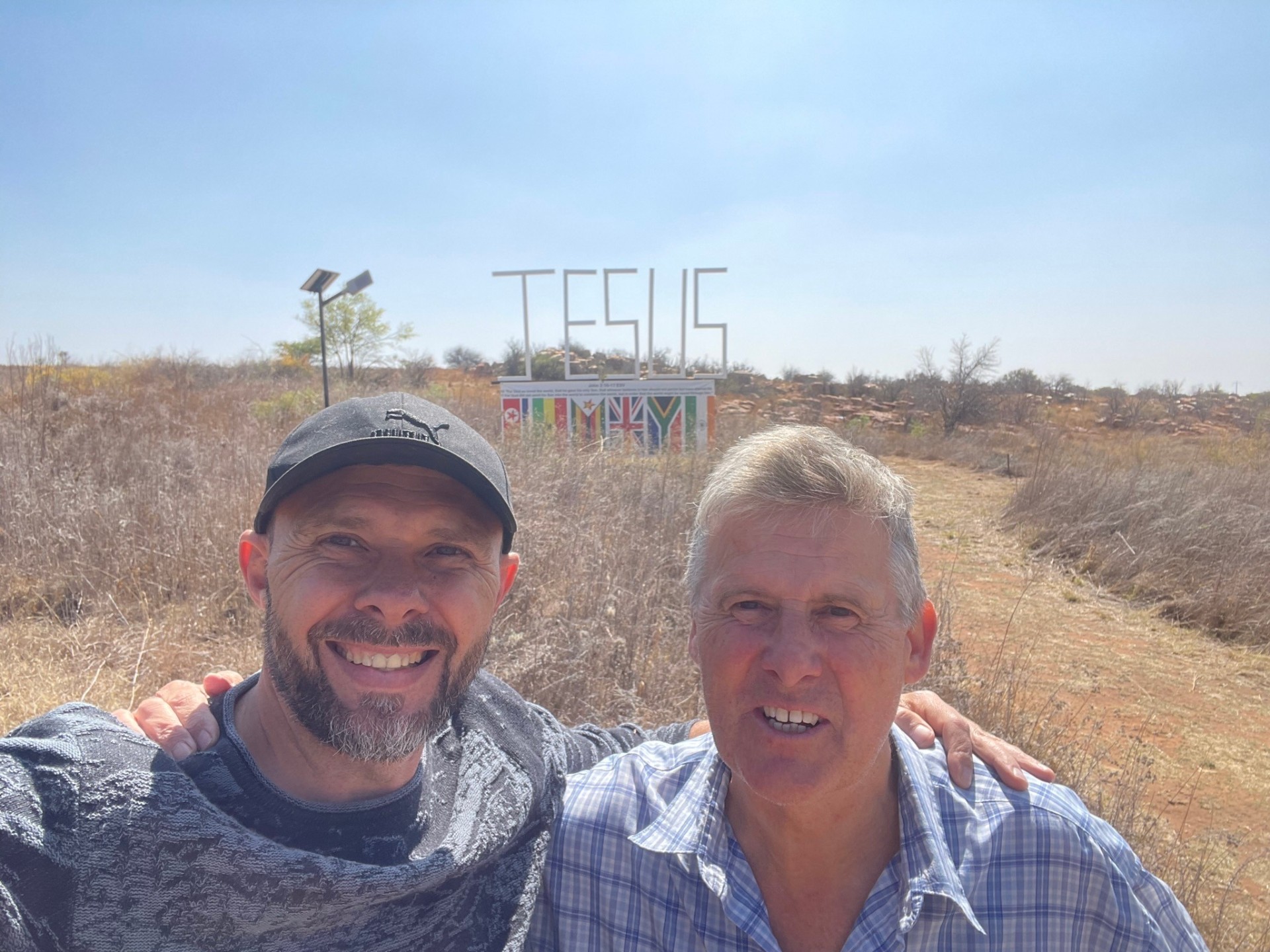 Two men selfie with the JESUS sign in the distance