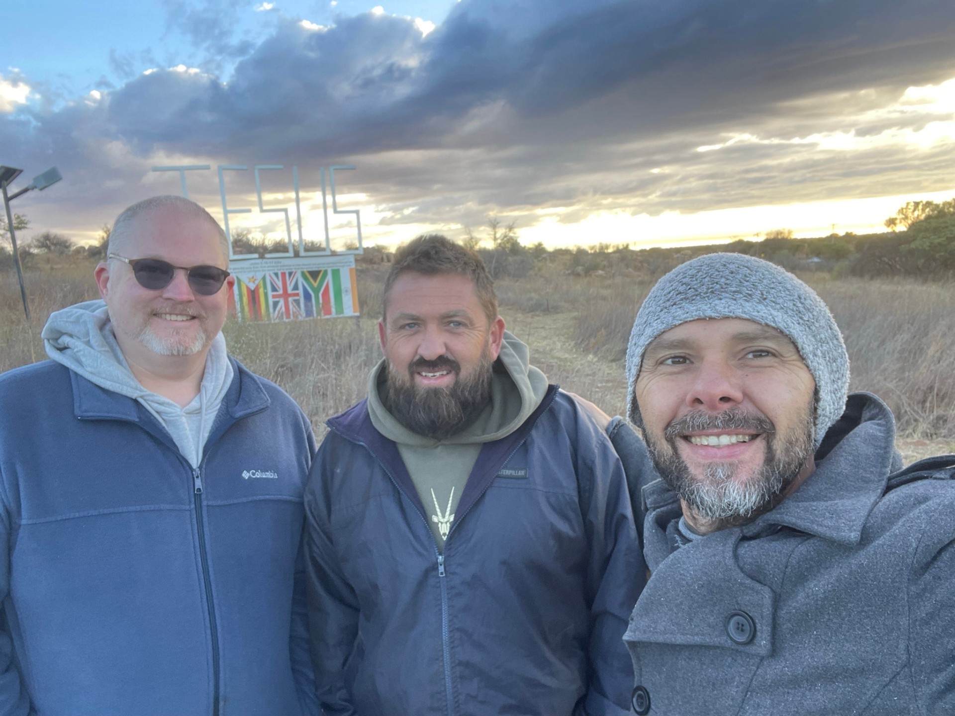 Three men selfie at sunset by the JESUS sign