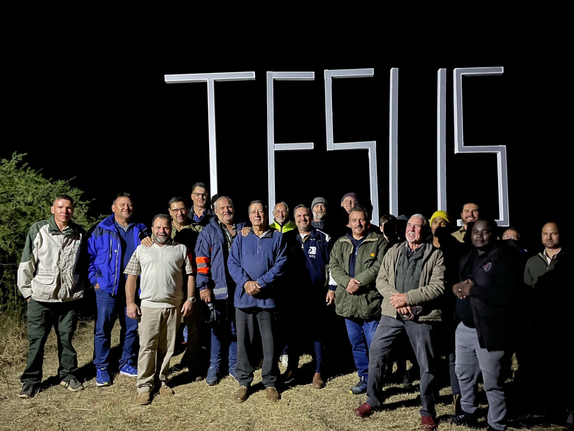Men's group photo at the JESUS sign at night