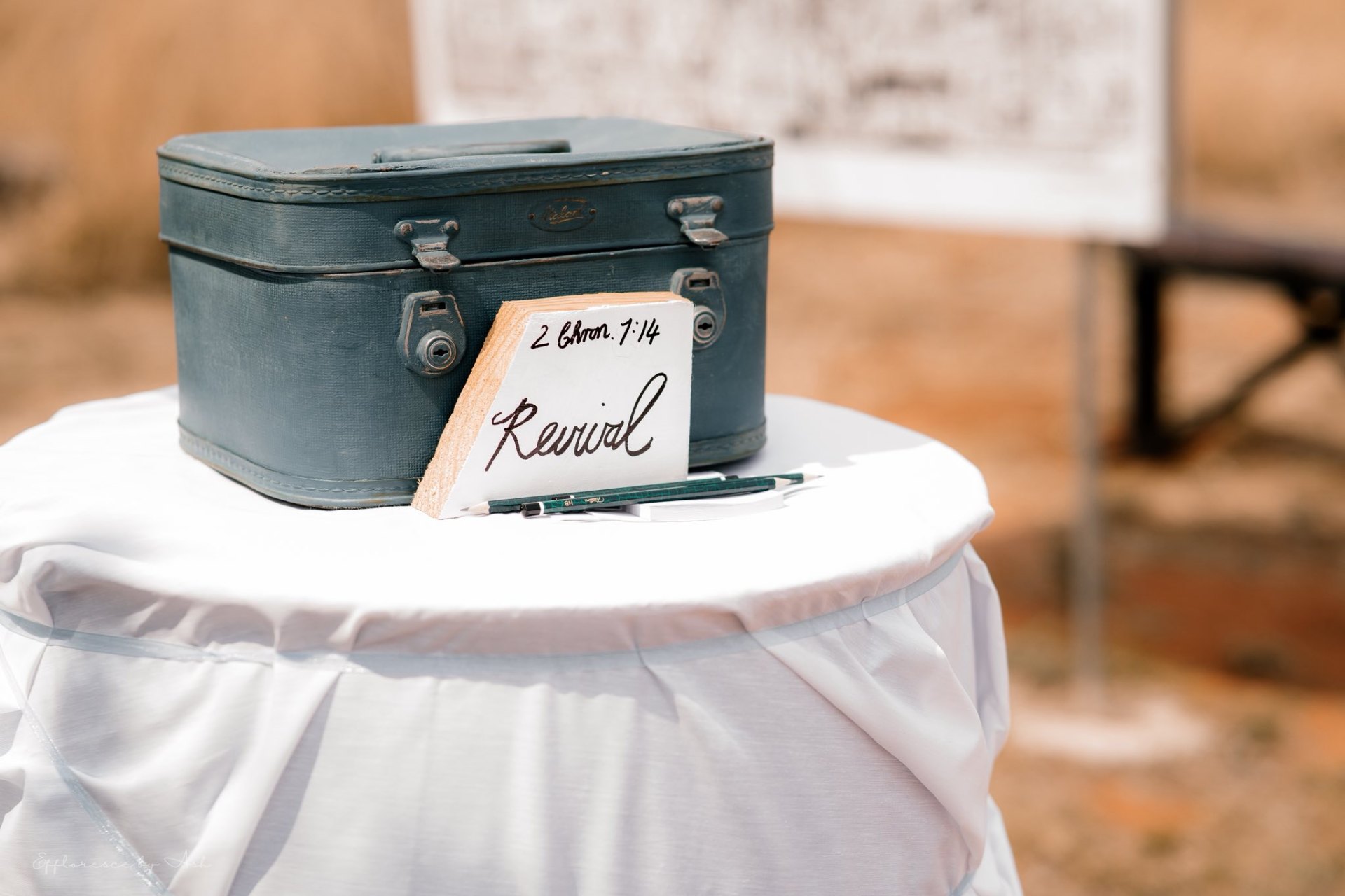 Vintage suitcase and 'Revival — 2 Chron 7:14' wooden card on a draped table