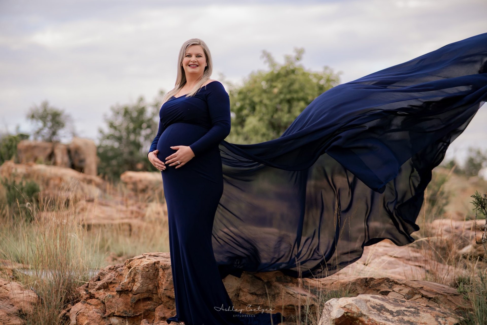 Maternity portrait with a flowing navy dress on the rocks