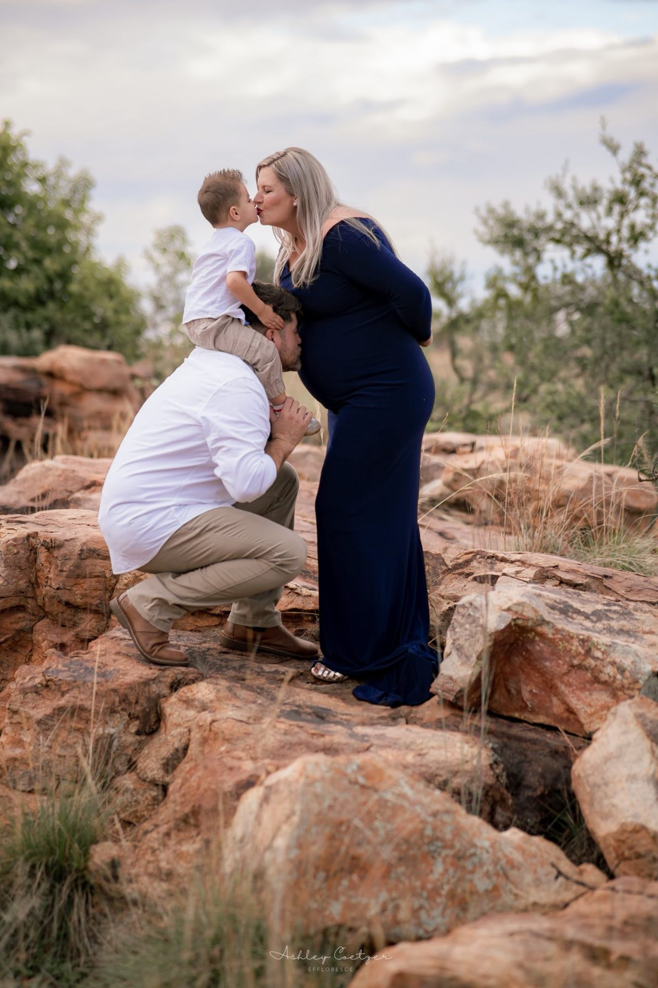 Maternity family moment — dad lifting toddler to kiss mom